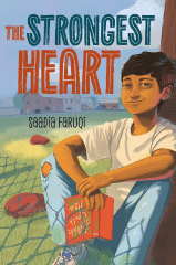 Boy smiling and sitting against a tree, holding a book with the shadow of a chain link fence on his legs and a large farm house in the background.