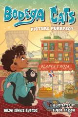 A young boy sits on a brick rooftop with his arm around a cat looking out at the city buildings and bridge against the sunset.