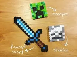 Perler bead crafts of a Minecraft sword, creeper and skeleton on a light wood table background.