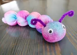 Tie dye pink and blue worm stuffed animal with googly eyes and purple pipe cleaner antennas on a wooden table.