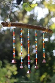 Green trees blurry in background. In foreground there is a wooden stick horizontal with strings of multicolored beads hanging off.