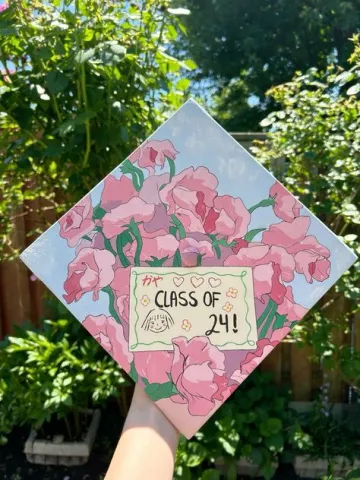Graduation cap painted with pink flowers and a painted letter in the middle that says "Class of '24"