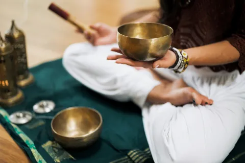 A photograph of a seated person holding a sound bowl