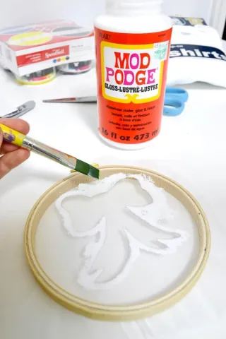 Person showing how to use mod podge to DIY screen print a bow
